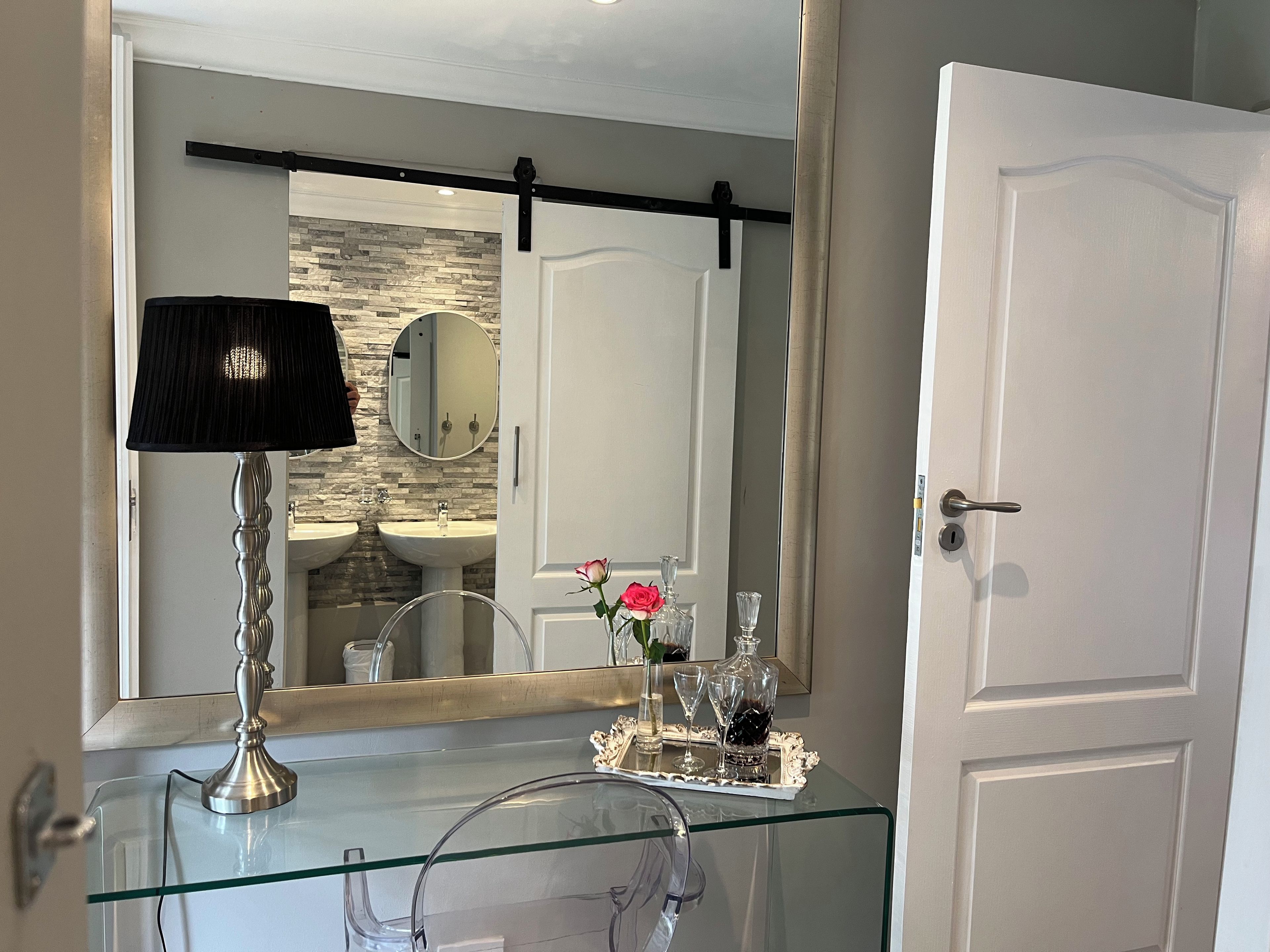 A bathroom with a glass vanity, a mirror, a black lamp, and a door.