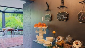 A dining area with a buffet table, clear chairs, and a view of greenery outside. - Patcham Place B&B (Clarens)