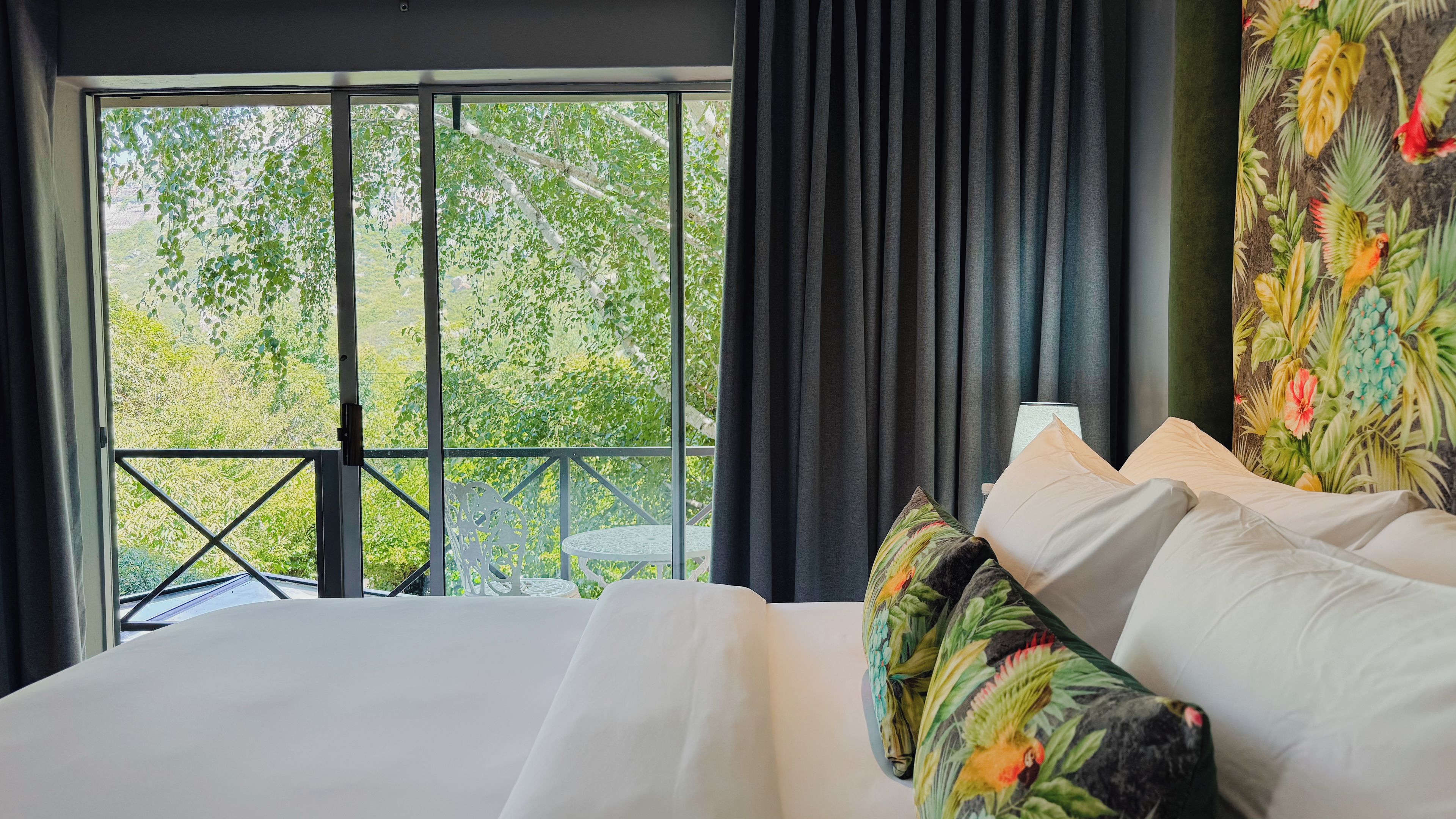 Quarto de hotel com uma janela ampla, cama com roupa de cama branca e vista para o verde lá fora.