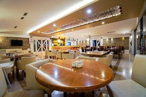 A modern restaurant with round tables and comfortable seating, a bar area, and a television screen on the wall. - Limapark Hotel (Serdivan)