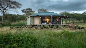 A tent with a covered porch, a table, and chairs, surrounded by greenery. - Ole Serai Luxury Camp (Bariadi)