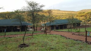 A campsite with tents and a small building, surrounded by grass and trees. - Ole Serai Luxury Camp (Bariadi)