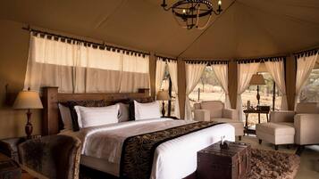 A tented room with a large bed, two chairs, a wooden nightstand, and a chandelier.