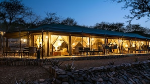 A spacious outdoor dining area with tables and chairs, surrounded by a stone wall and plants. - Ole Serai Luxury Camp (Bariadi)