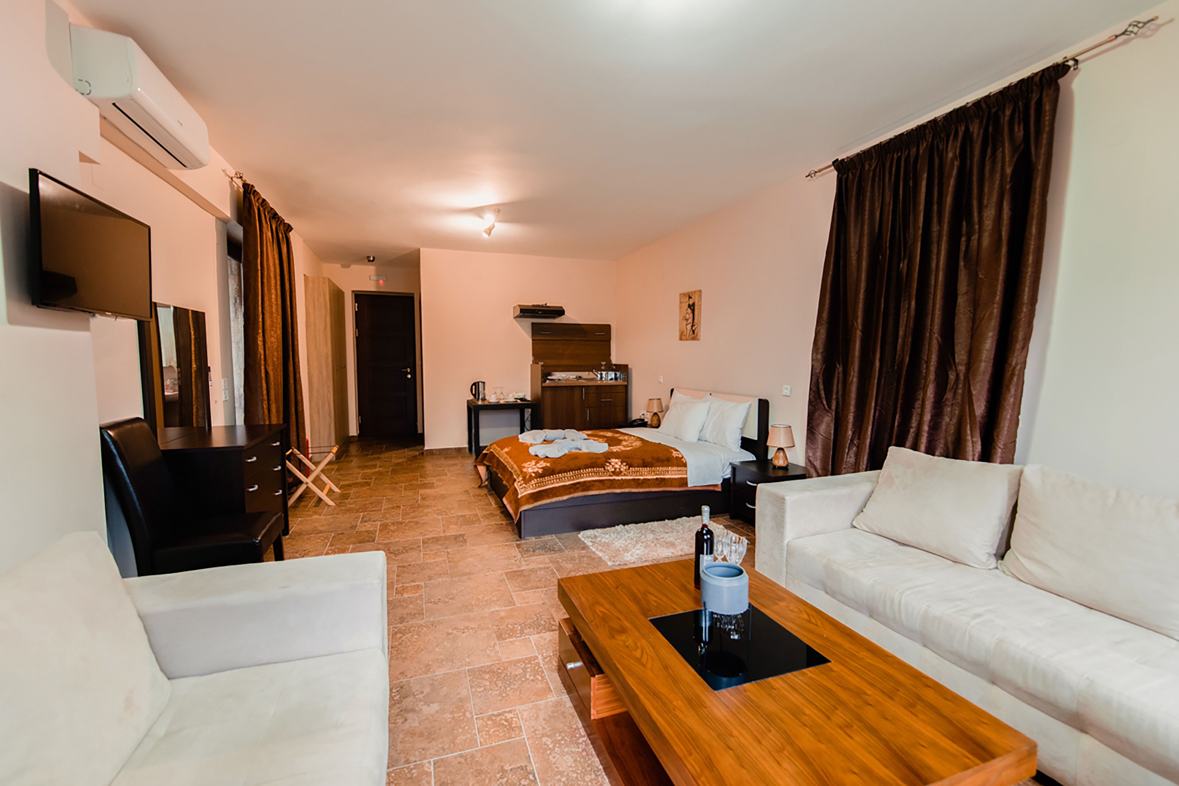 A hotel room with a bed, a sofa, a TV, a desk, and a coffee table.