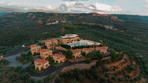 Vista aérea de un complejo turístico con varias construcciones de piedra, una piscina y un camino sinuoso.