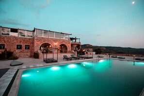 A pool area with lounge chairs and a stone building with arched windows. - Melies Hotel (Sparta)
