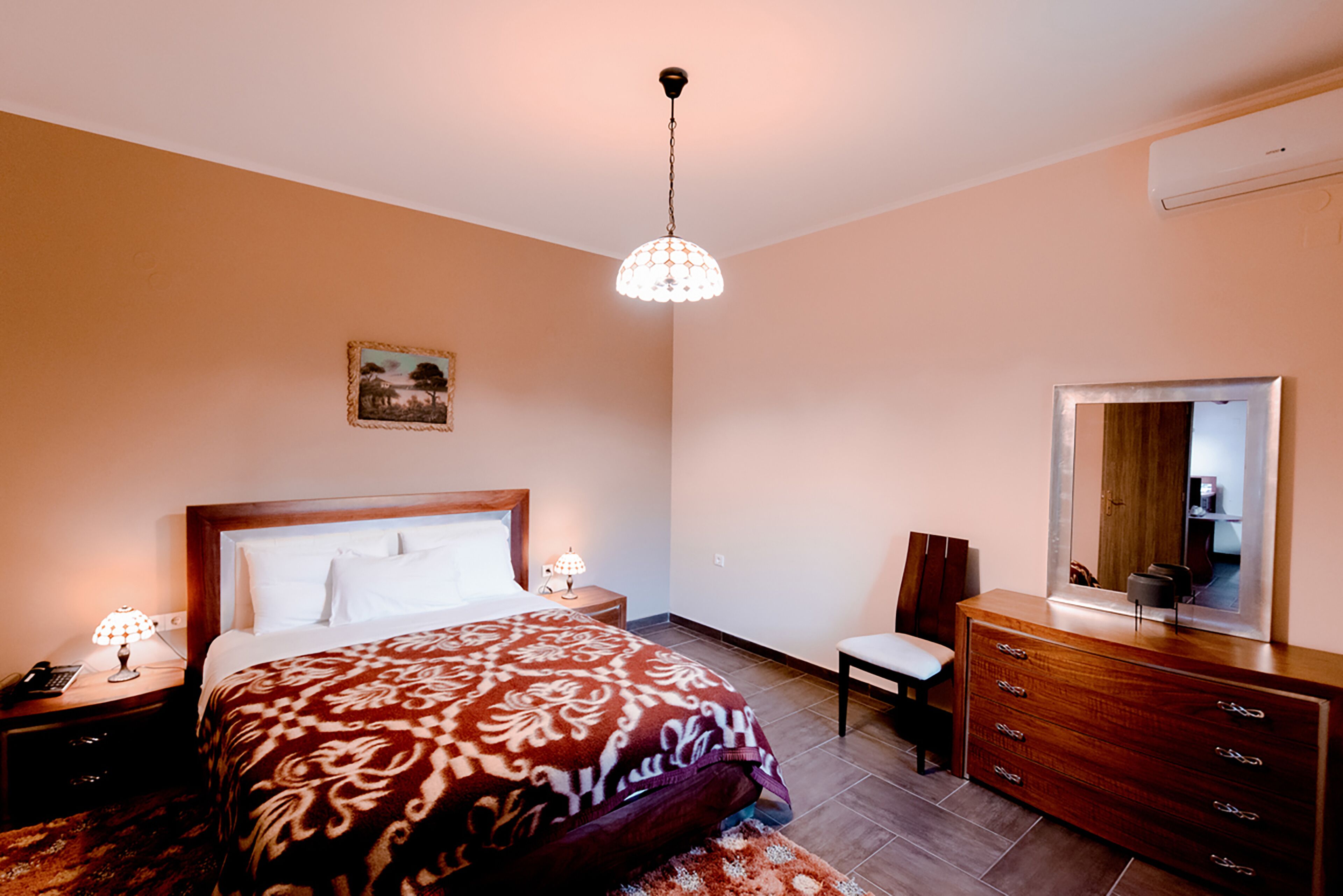 Quarto com cama, abajures, cómoda, cadeira e luminária suspensa.
