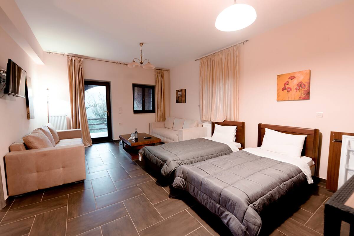 A hotel room with a sofa, two beds, a wooden nightstand, and a painting on the wall.