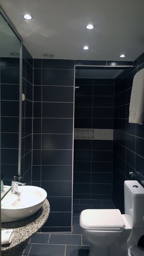 A modern bathroom with dark tiles, a white sink, and a toilet. - Hôtel M'lys (Conakry)