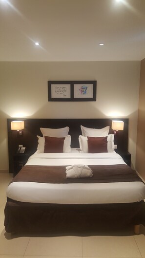 A hotel room with a large bed, two bedside lamps, a framed quote, and a folded towel on the bed. - Hôtel M'lys (Conakry)