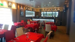A restaurant with red tablecloths, multiple framed pictures on the walls, and a stone wall feature. - Hôtel M'lys (Conakry)