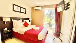 A hotel room with a bed, nightstand, and a TV mounted on the wall. - Hôtel M'lys (Conakry)