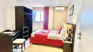 A hotel room with a bed, desk, chair, wardrobe, and a window with curtains. - Hôtel M'lys (Conakry)