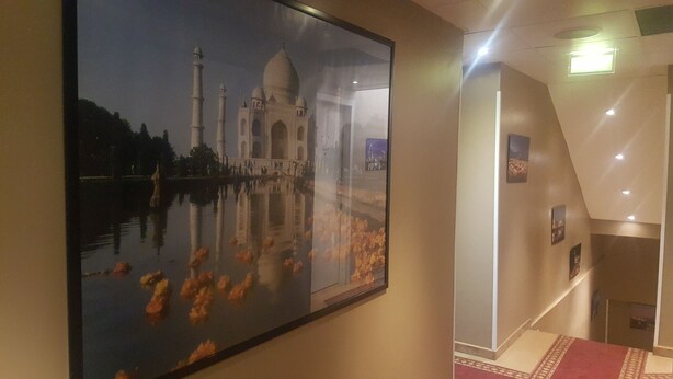 A framed photograph of the Taj Mahal with a reflection in water, a staircase, and a wall with a framed picture. - Hôtel M'lys (Conakry)
