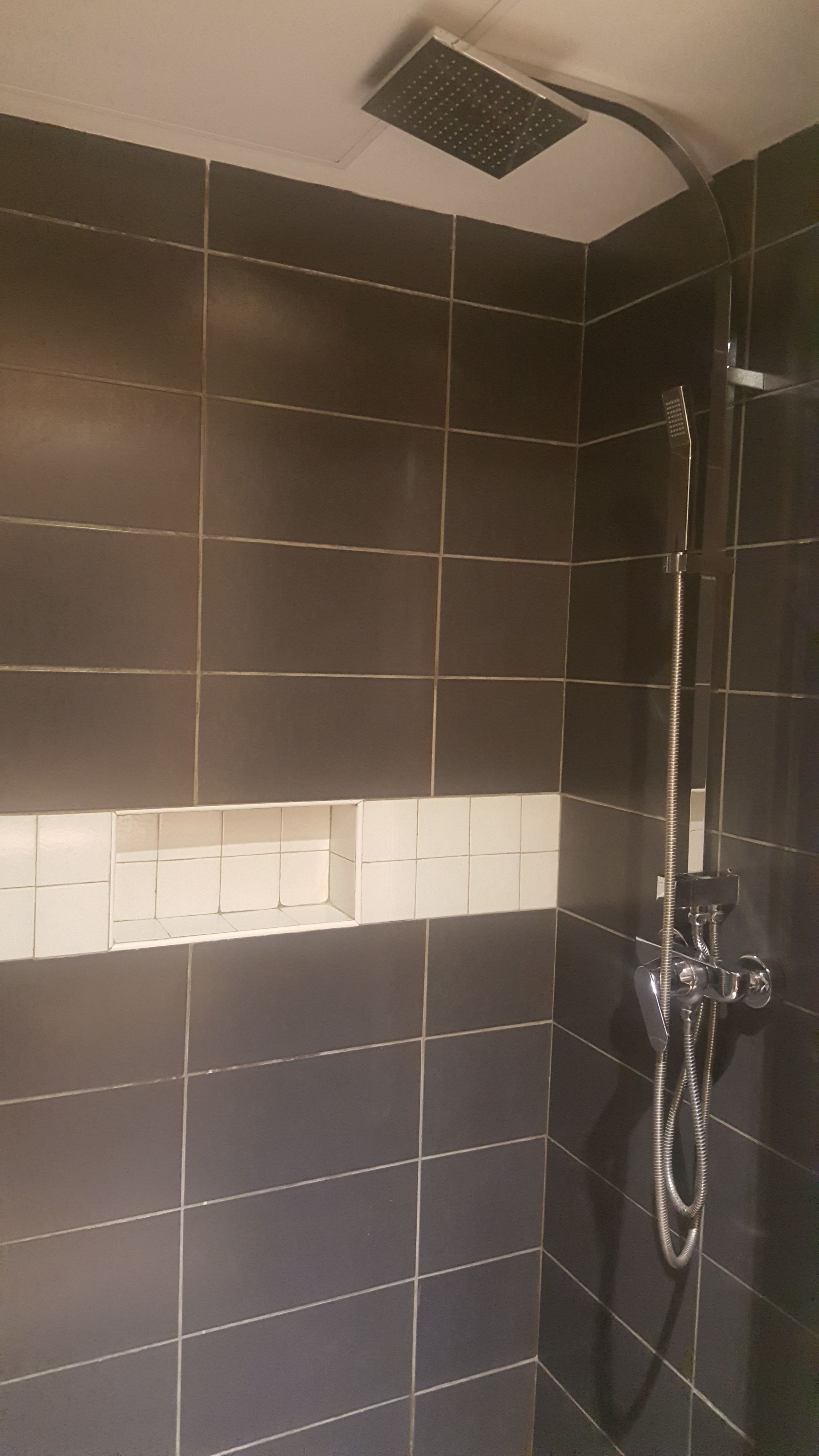 A bathroom with dark tiled walls, a white tiled accent wall, and a shower with a handheld showerhead.