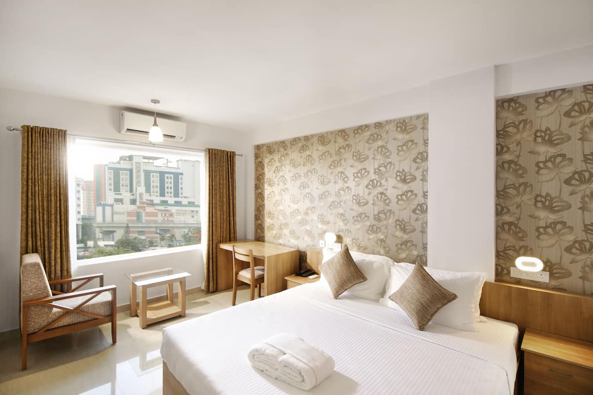 A hotel room with a bed, a desk, a chair, a nightstand, and a window with curtains.