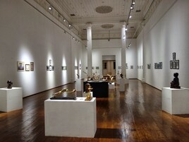 Una galería de arte con paredes blancas, suelos de madera e iluminación en el techo.
