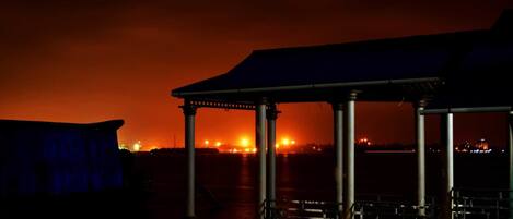 A covered outdoor area with a metal structure, possibly a gazebo, overlooking a cityscape with visible lights in the distance.