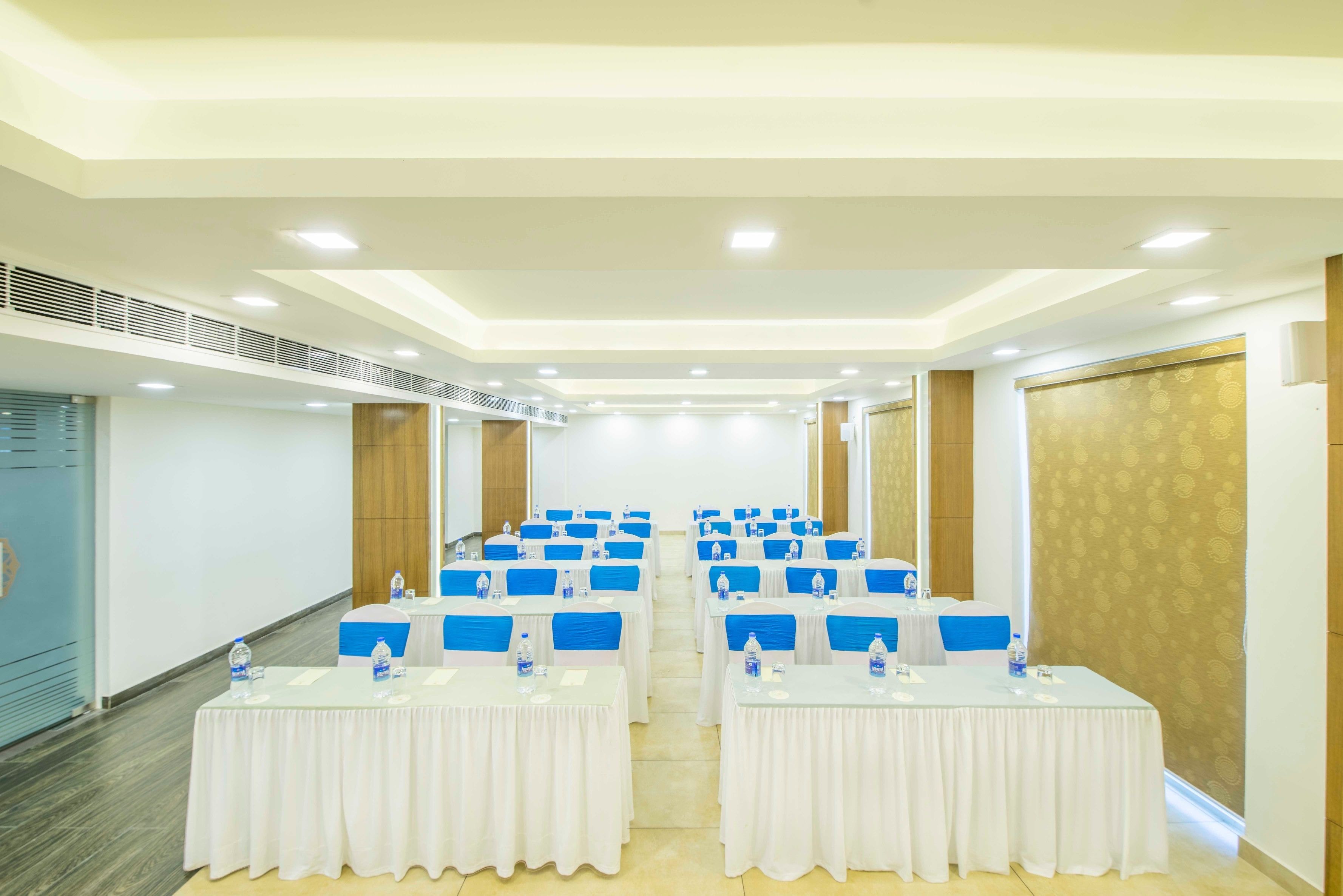 A conference room with rows of tables, each with a white tablecloth and blue chairs, equipped with water bottles.