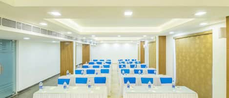 A conference room with rows of tables, each with a white tablecloth and blue chairs, equipped with water bottles.
