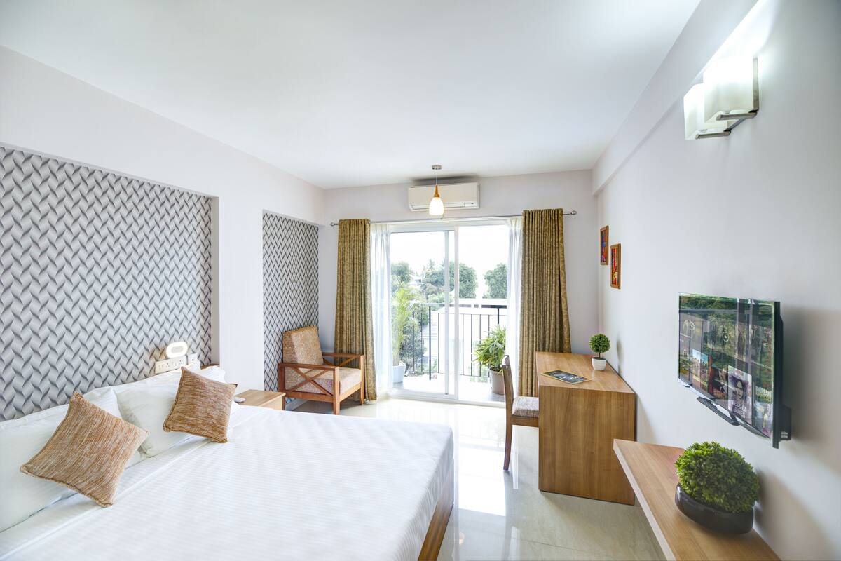 A hotel room with a bed, desk, chair, and a TV mounted on the wall.