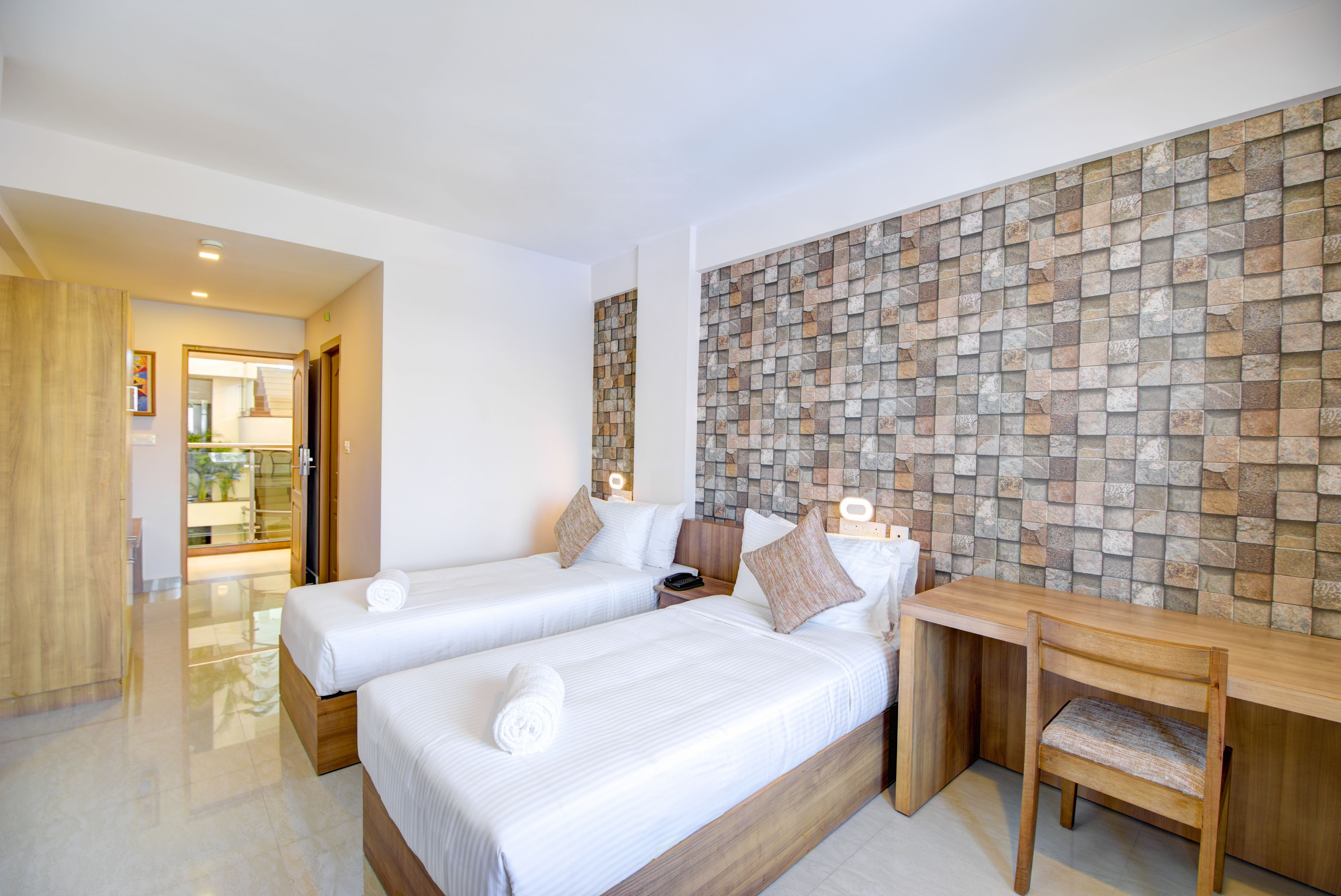 Habitación de hotel con dos camas, un escritorio de madera y una pared con diseño de piedra.