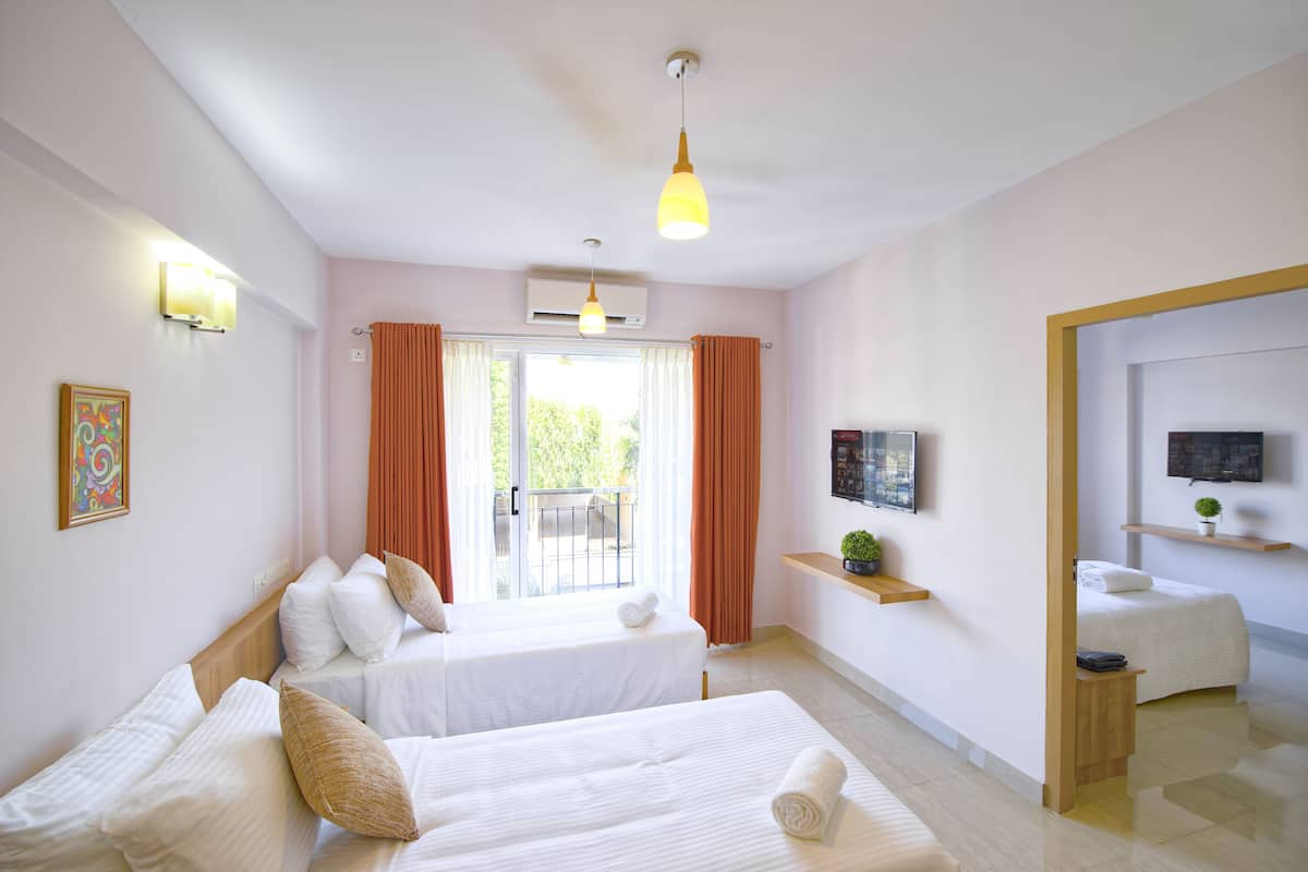 A hotel room with two beds, a TV, a small plant, and a balcony with curtains.