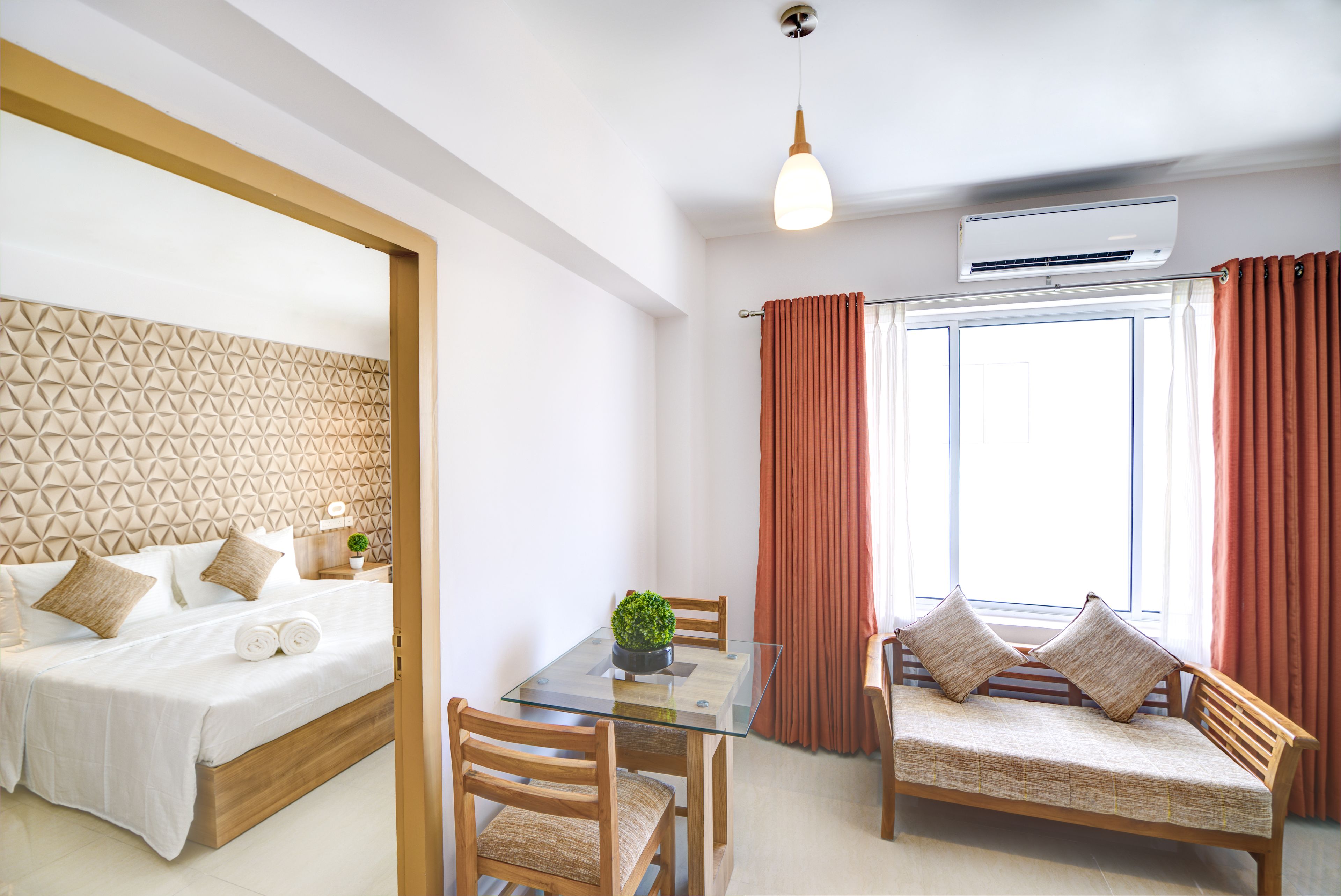 A modern hotel room with a bed, a glass dining table, a sofa, and a window with curtains.