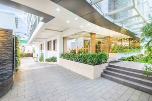 Una entrada de hotel moderna con fachada de vidrio, zona de estar al aire libre y pared de piedra.