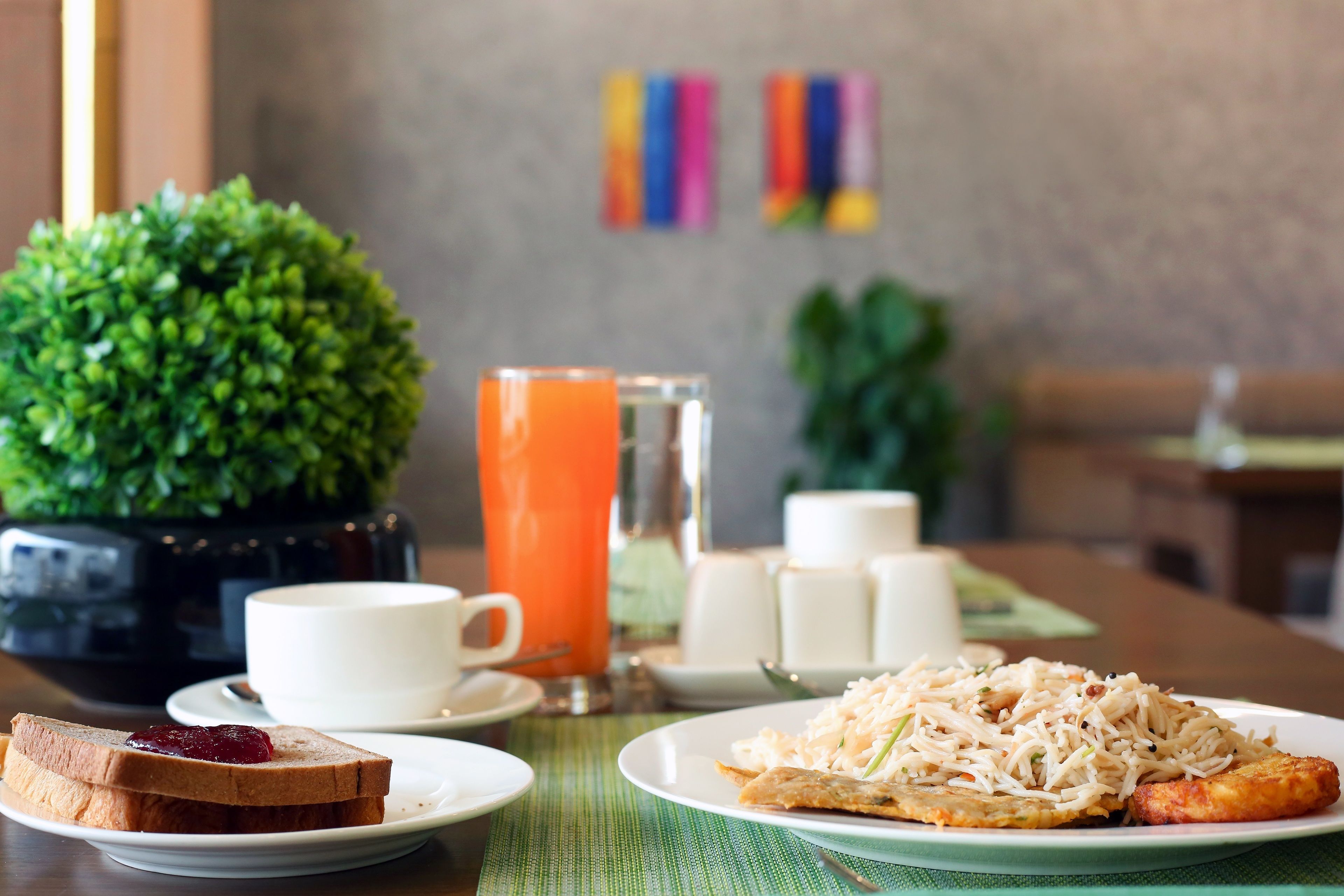 A breakfast setting with toast, a plate of rice with vegetables, a glass of orange juice, and a cup of coffee on a table with a green placemat.
