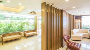 A modern lobby with a glass wall, wooden benches, a leather chair, and a beige sofa. - Sidra Pristine Hotel & Portico Halls (Kanayannur)
