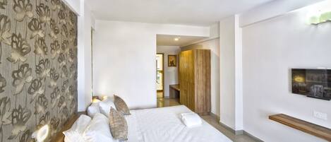 Habitación de hotel con cama, cabecera de madera, televisor montado en la pared y estante de madera.