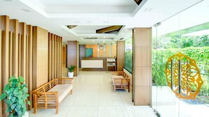 A modern reception area with wooden paneling, a reception desk, seating arrangements, and a large window offering a view of greenery. - Sidra Pristine Hotel & Portico Halls (Kanayannur)