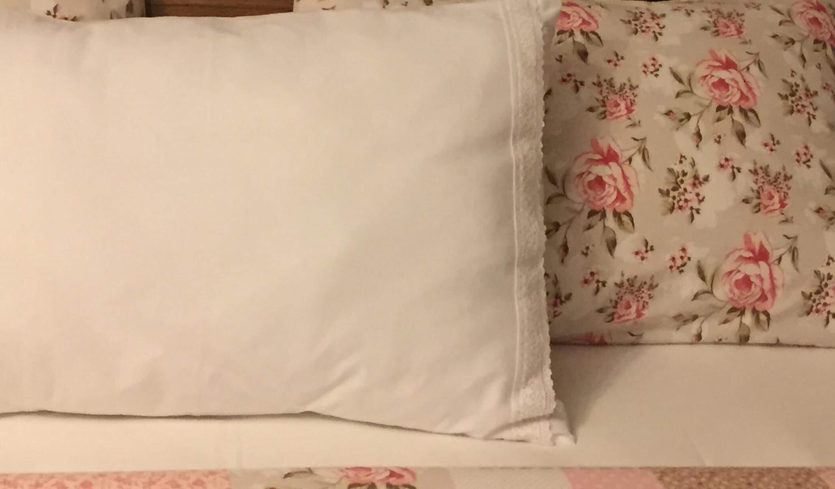 A bed with a plain white pillow and a floral-patterned pillow.