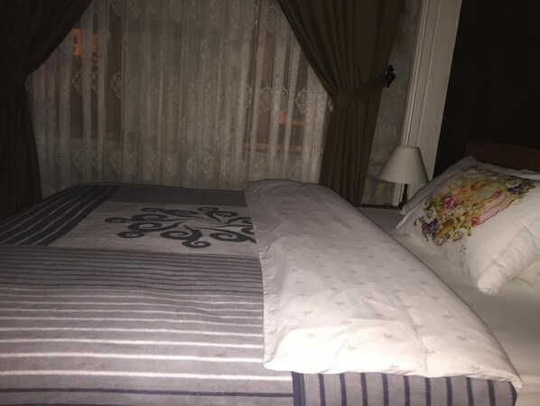 A bed with a striped bedspread and a floral pillow, a bedside lamp, and sheer curtains.