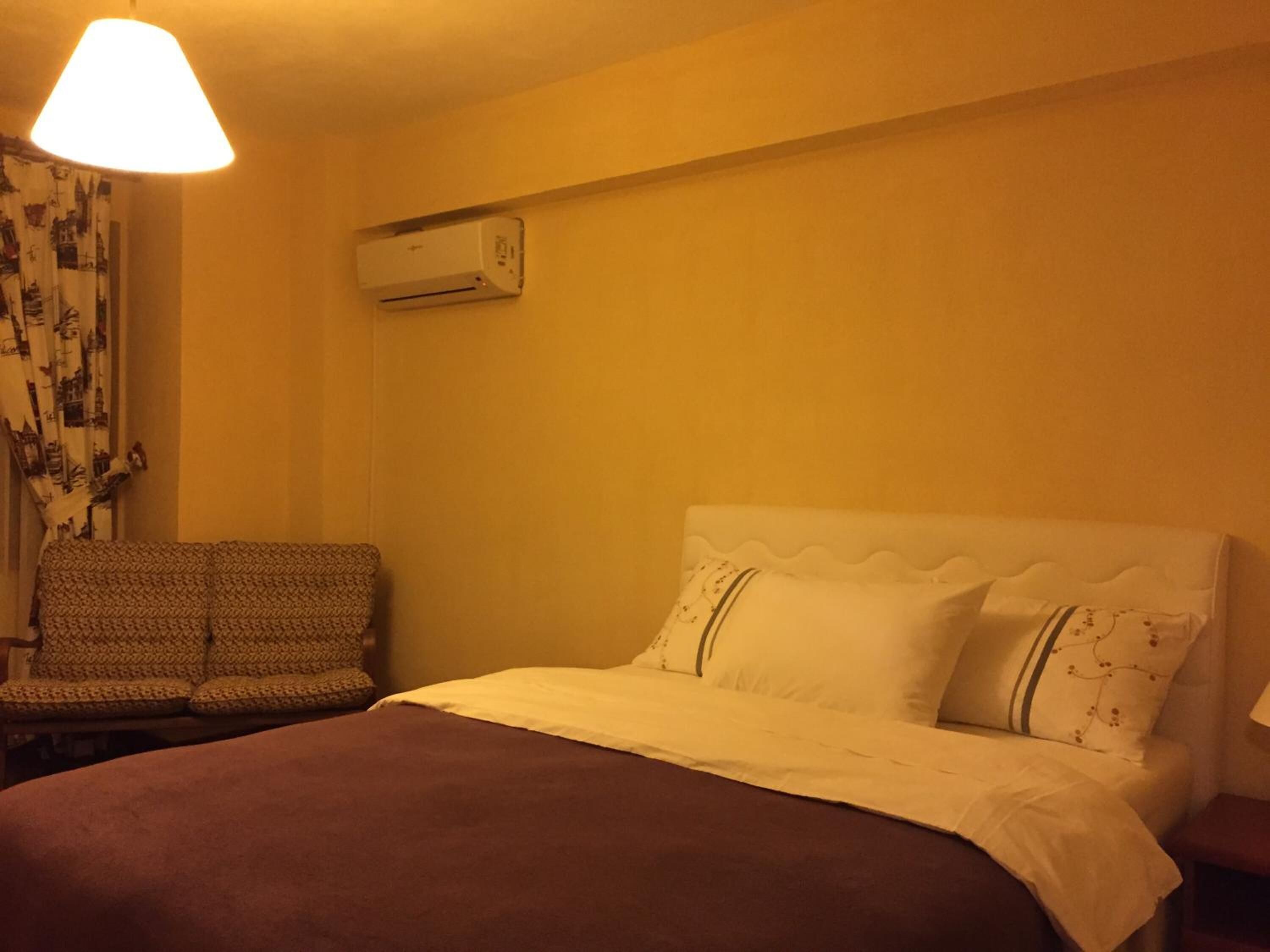 Quarto de hotel com uma cama, uma cadeira, um ar condicionado e um abajur.
