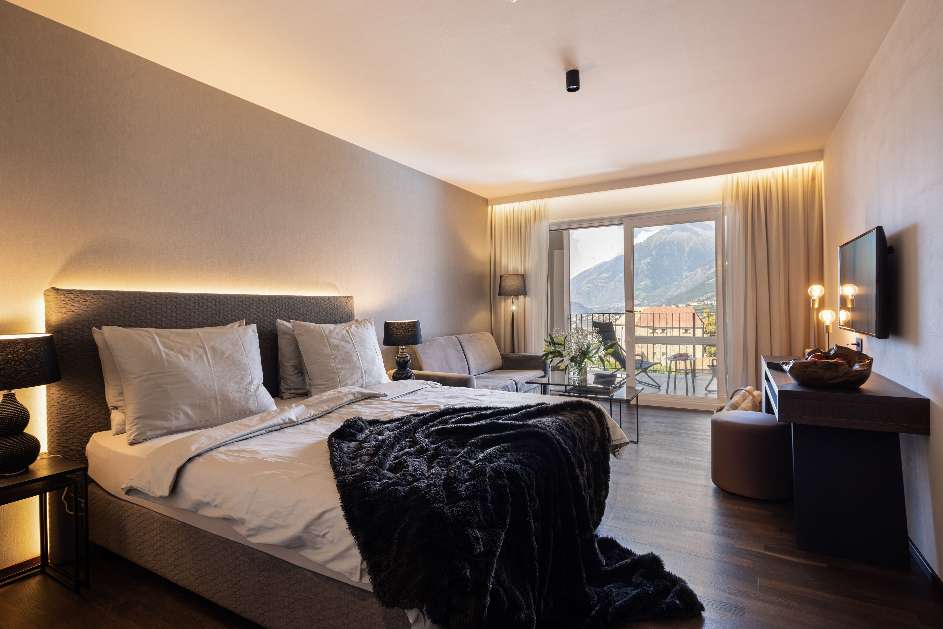 Una habitación de hotel moderna con una cama grande, un sofá, un escritorio y un balcón con vista a la montaña.