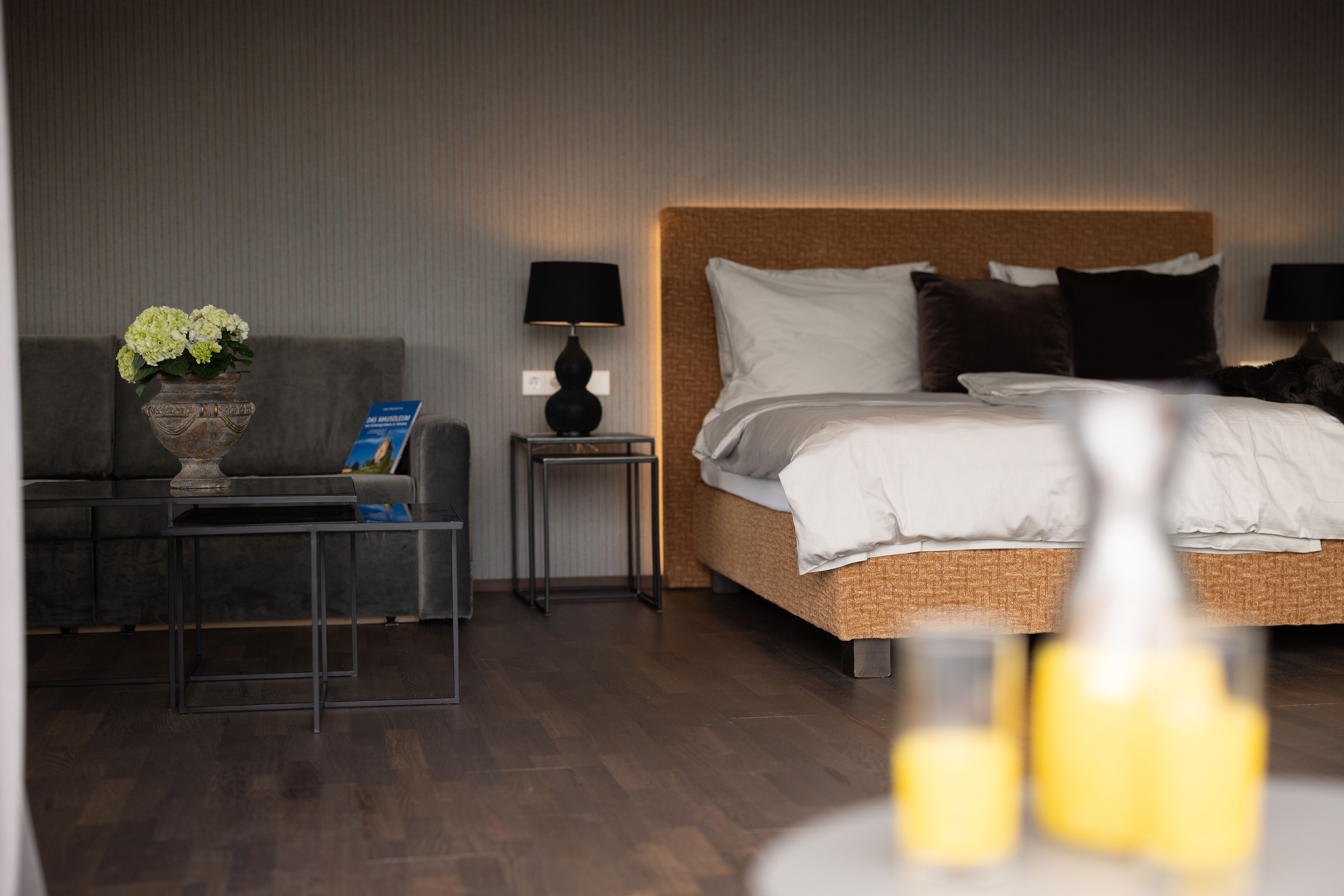 A modern hotel room with a large bed, a sofa, a small side table, and a lamp.