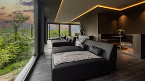 A modern living room with a large sofa set, a dining area, and a view of greenery. - Hotel Finkenhof (Schenna)