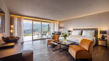 Habitación de hotel moderna con una cama grande, una zona de estar con una mesa de centro y vistas a las montañas desde el balcón.