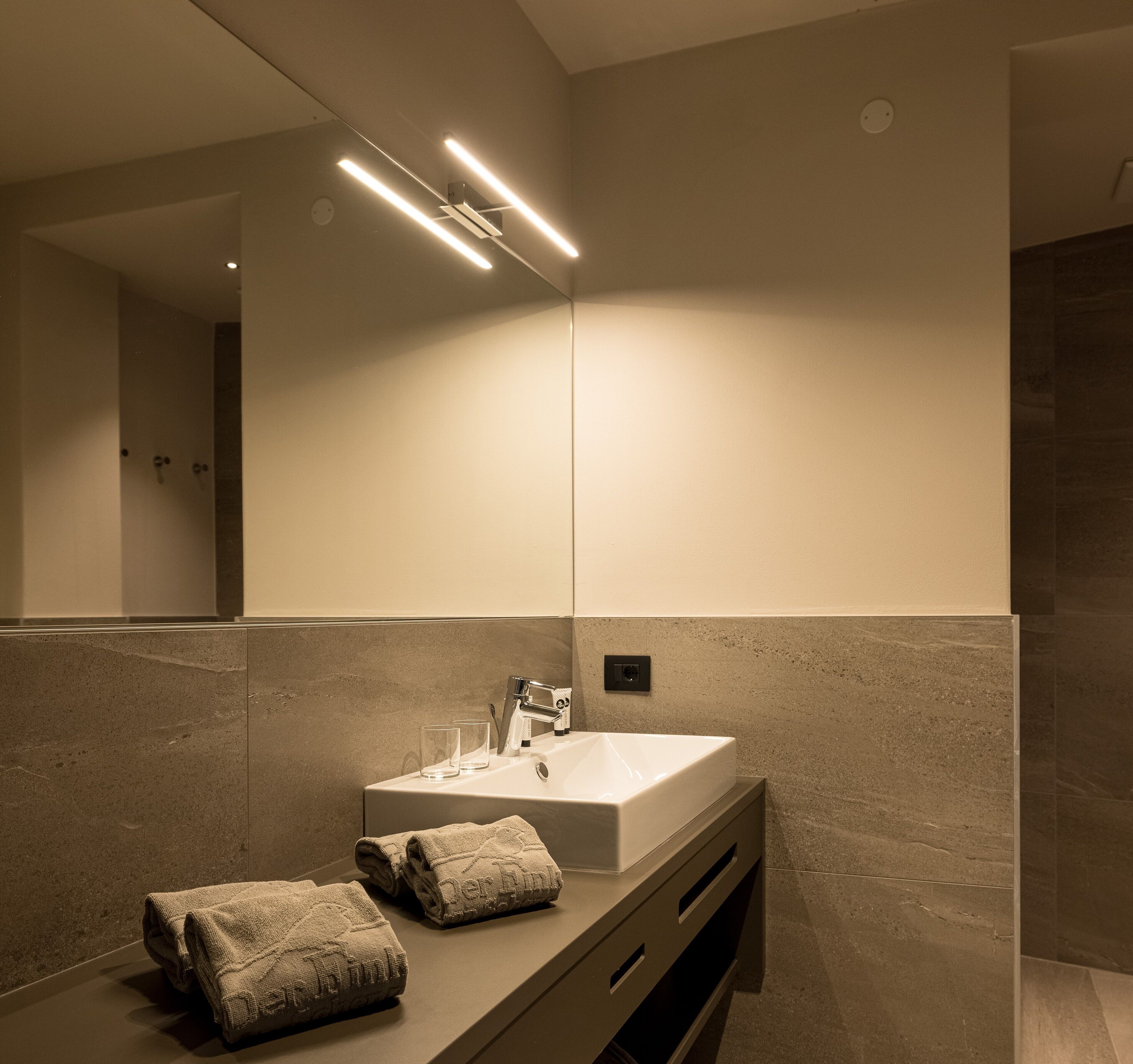 A modern bathroom with a large mirror, a white sink, and a towel on the counter.