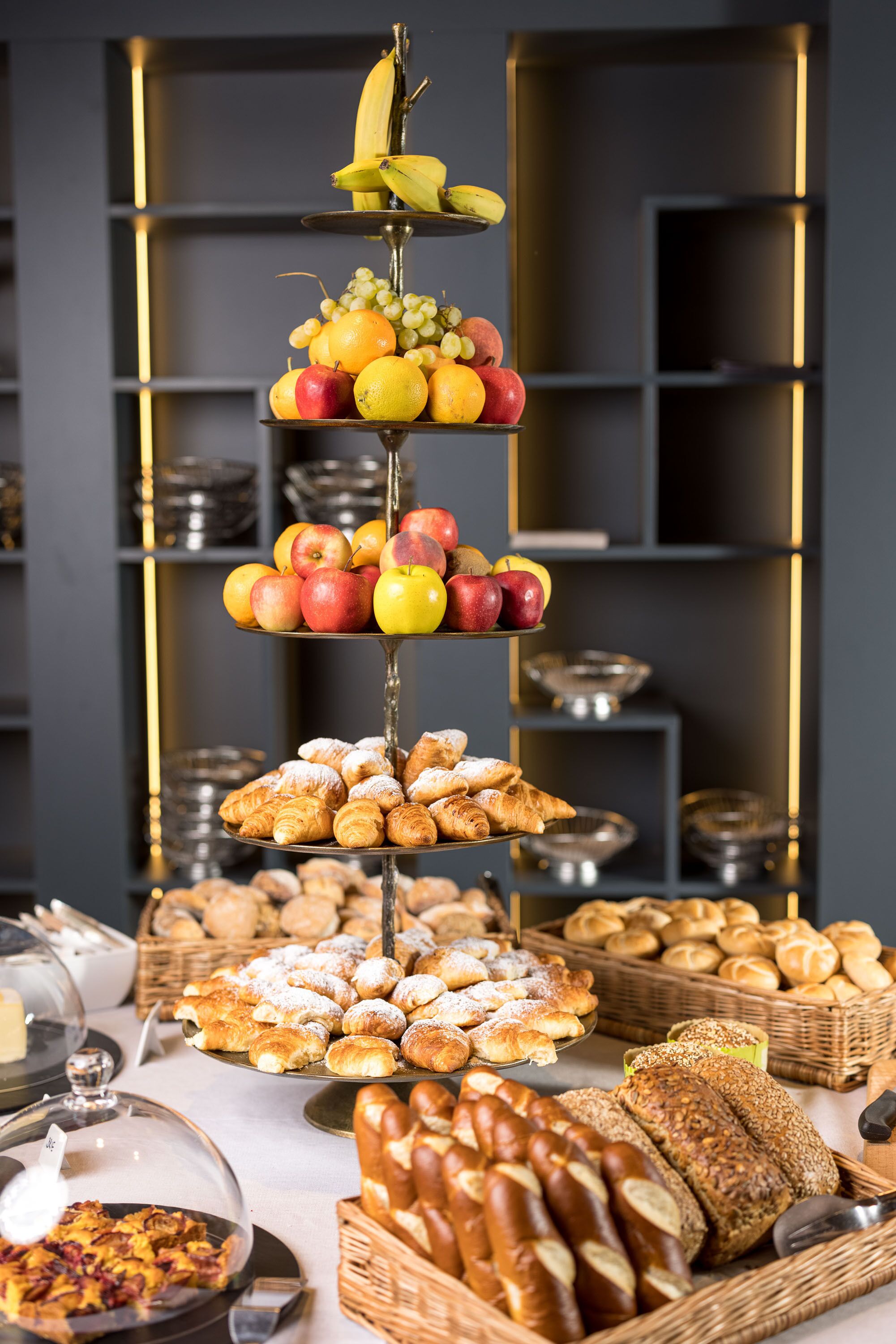 A multi-tiered fruit and pastry display with baskets of bread and pastries in the foreground.