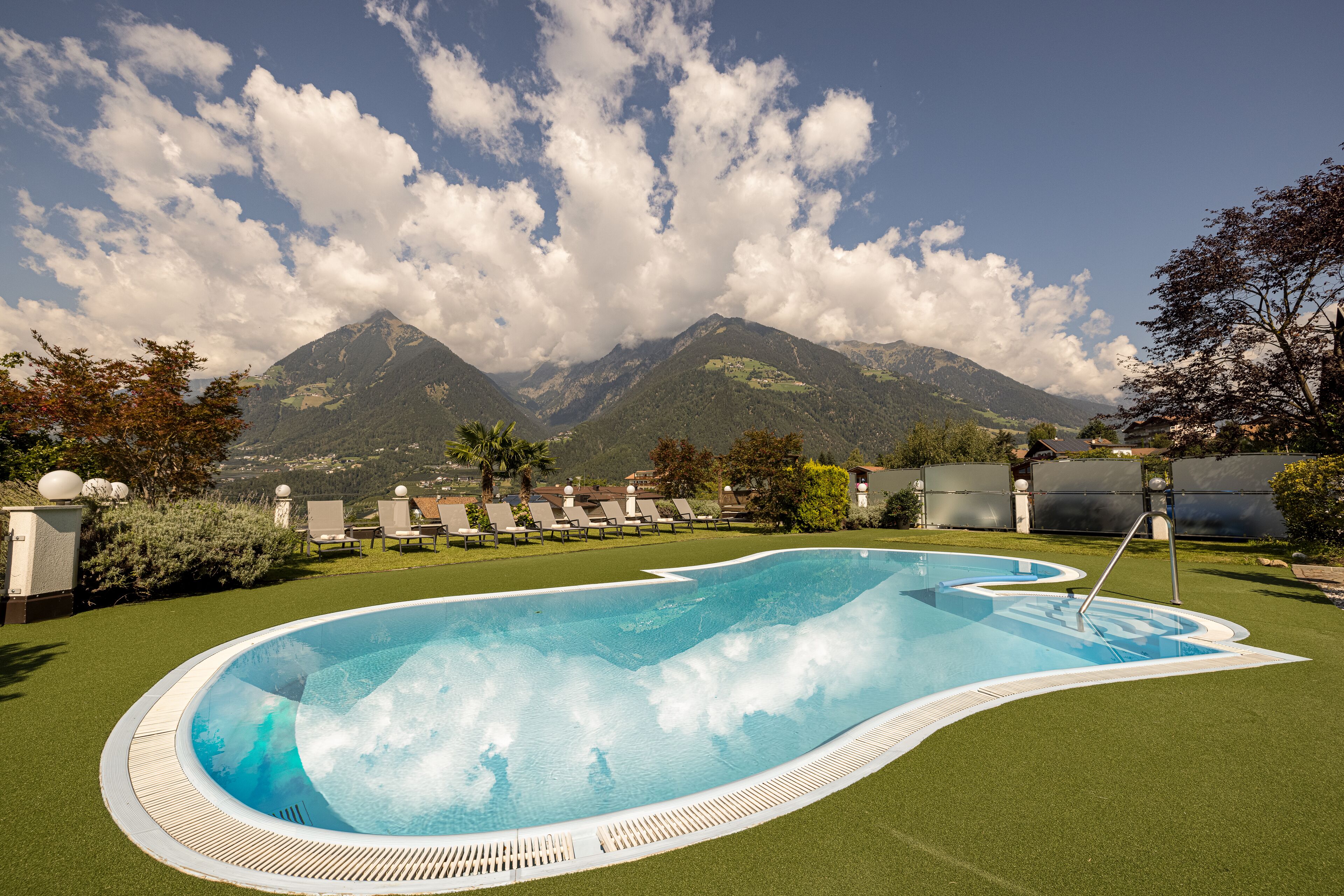 A swimming pool with a view of mountains, surrounded by lounge chairs and a well-maintained lawn.