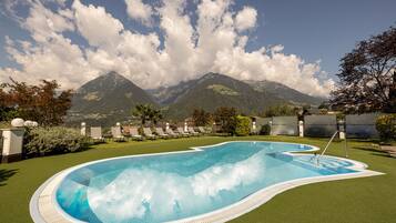 A swimming pool with a view of mountains, surrounded by lounge chairs and a well-maintained lawn.