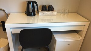 Une petite cuisine équipée avec un plan de travail blanc, une bouilloire électrique noire, une machine à café et un mini-réfrigérateur.
