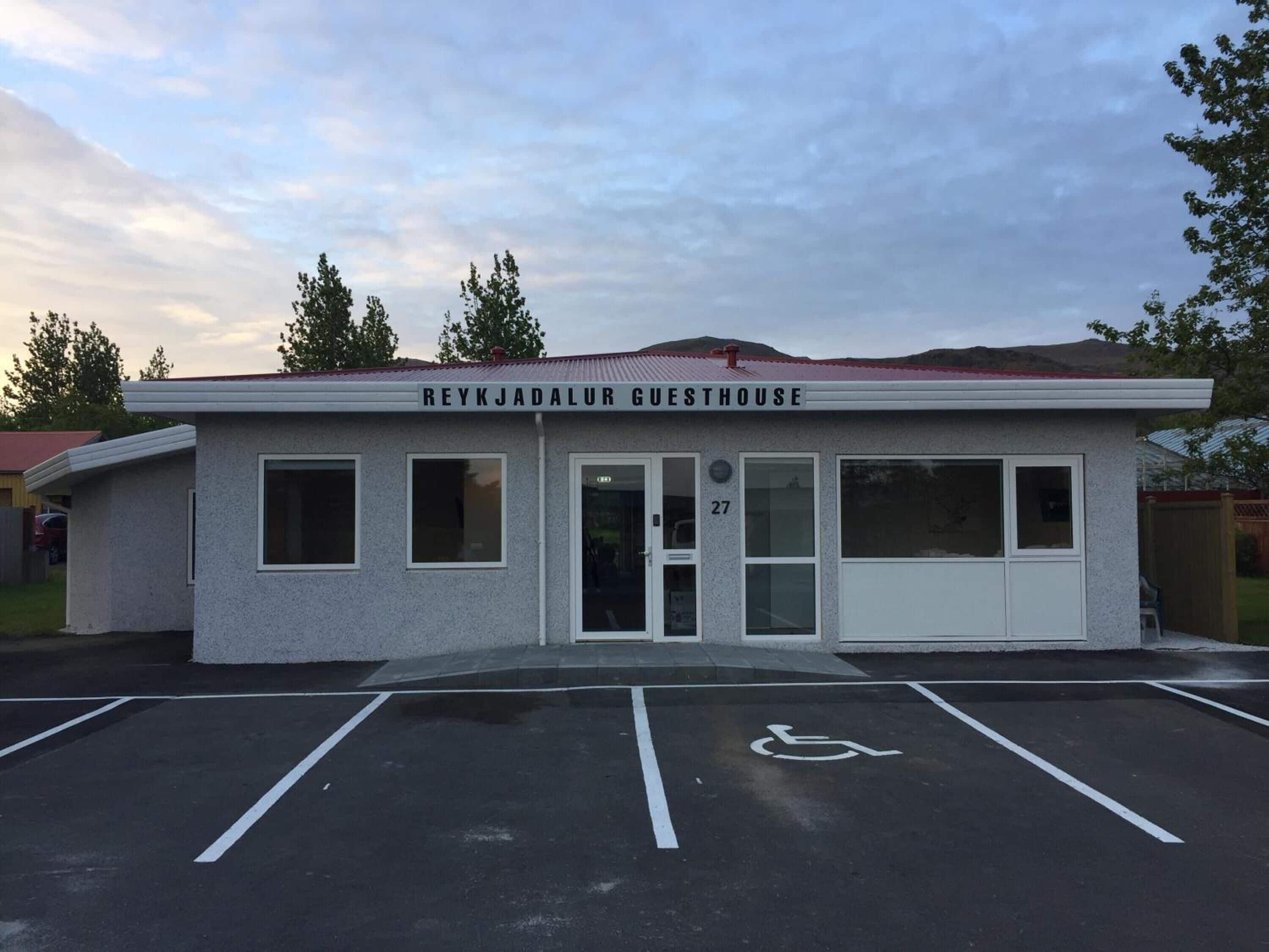 Una casa de huéspedes llamada REYKJADALUR GUESTHOUSE, con un letrero con el número 27, un espacio de estacionamiento accesible para sillas de ruedas y un techo rojo.