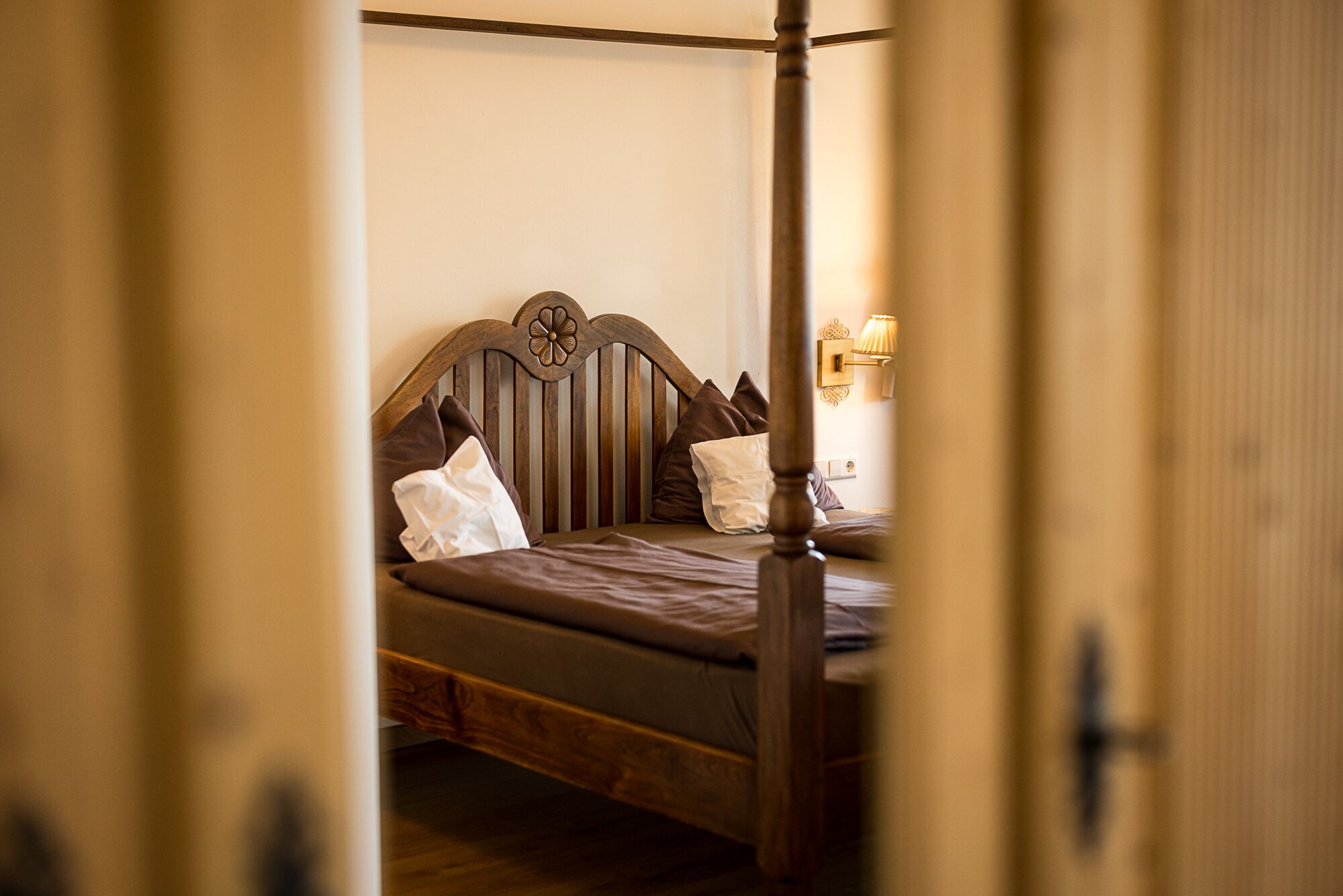 Un lit à baldaquin en bois, doté d’une tête de lit, d’oreillers et d’une table de chevet avec une lampe.