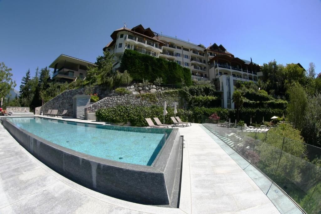 Una piscina con sillas de descanso, una pared de piedra y un edificio de hotel al fondo.