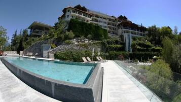 Una piscina con sillas de descanso, una pared de piedra y un edificio de hotel al fondo.